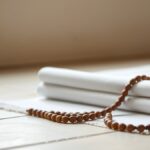 Ilustrasi sajadah putih polos terlipat dengan tasbih kayu di atas lantai batu