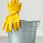 Ilustrasi sepasang sarung tangan karet kuning di tepi ember logam