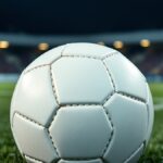 Ilustrasi bola sepak putih polos di dekat titik penalti lapangan rumput pada malam hari